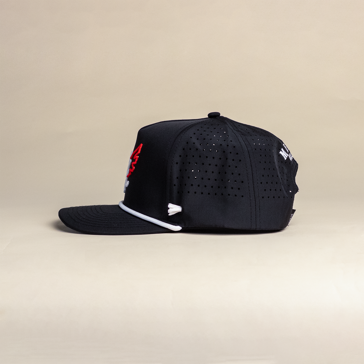 A black structured golf cap with a curved brim, featuring a red embroidered logo on the front, a golf tee holder on the side, and a white rope detail along the brim, photographed against a solid beige background.